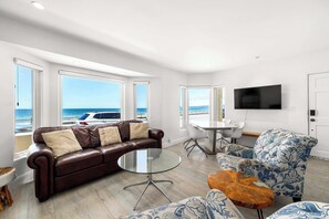 A modern living room with a leather sofa, a patterned armchair, a glass coffee table, and a dining area with a white table and chairs.