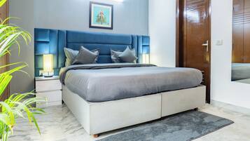 A modern bedroom with a large bed, two bedside tables with lamps, a blue headboard, a framed picture on the wall, and a wooden door.