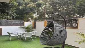 A hanging chair with a geometric pattern, a round table with chairs, and a small potted plant.