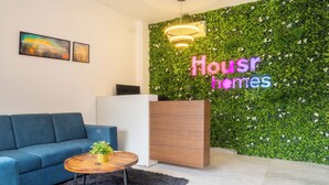 A modern reception area with a green wall, a neon sign reading "Housr homes," a blue sofa, and a wooden table with a plant.