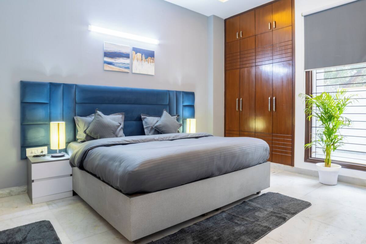 A modern bedroom with a large bed, a nightstand, a wardrobe, and a window with blinds.