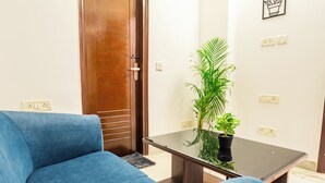 A living room with a blue sofa, a glass-top coffee table with a potted plant, and a wooden door.
