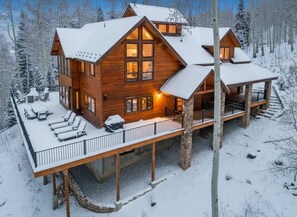 A large wooden cabin with multiple windows, a covered deck, and a snow-covered landscape. - Luxury Mountain Retreat with Hot Tub and Views (Telluride)
