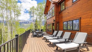 A wooden deck with lounge chairs and a table, overlooking a mountainous landscape. - Luxury Mountain Retreat with Hot Tub and Views (Telluride)