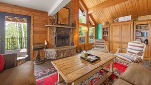 A cozy log cabin interior with a stone fireplace, wooden furniture, and a view of the outdoors. - Luxury Mountain Retreat with Hot Tub and Views (Telluride)