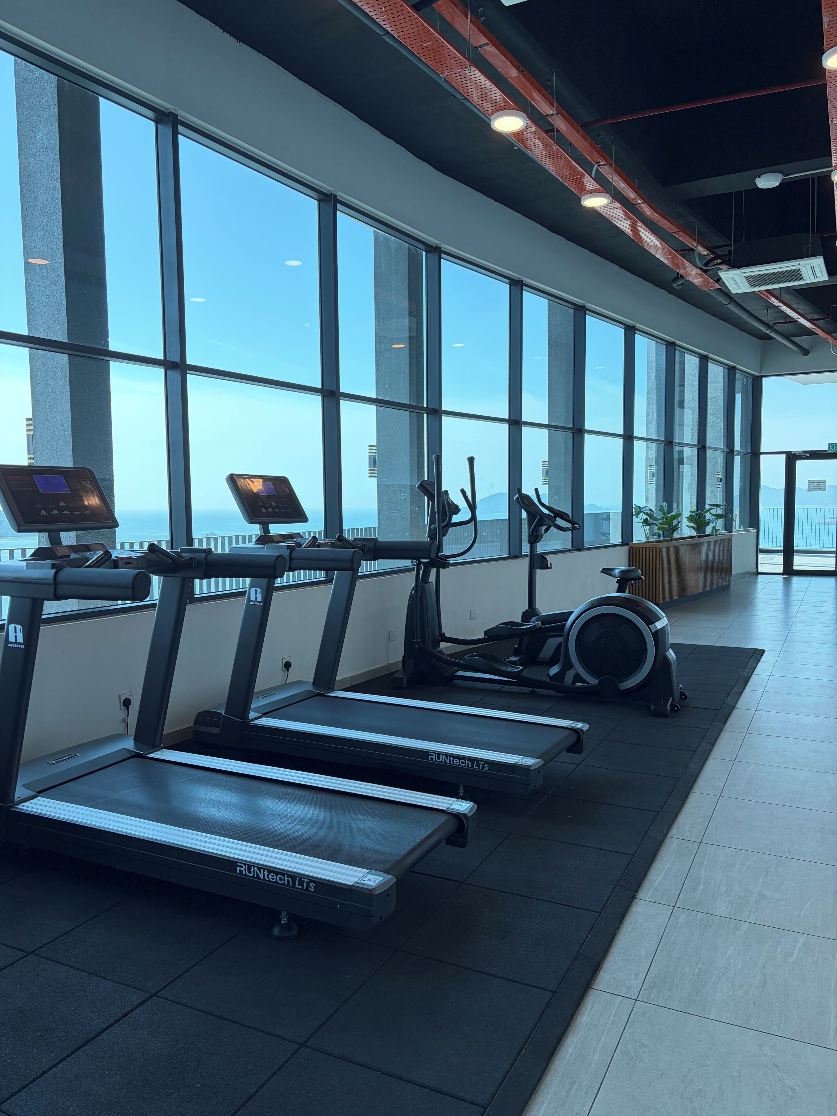 A gym with treadmills, an elliptical, and exercise bikes, large windows, and a view of the city.