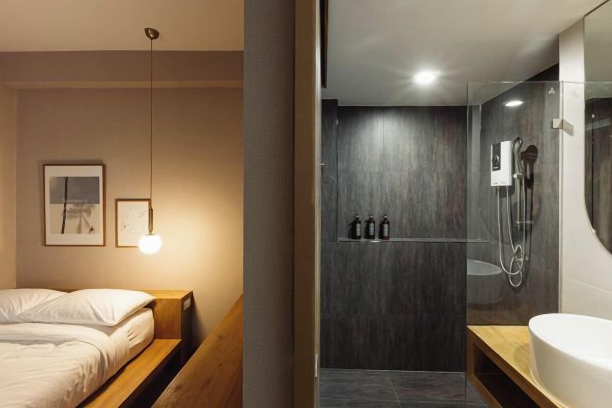 A modern bedroom with a wooden headboard, a bedside table, and a hanging light fixture.