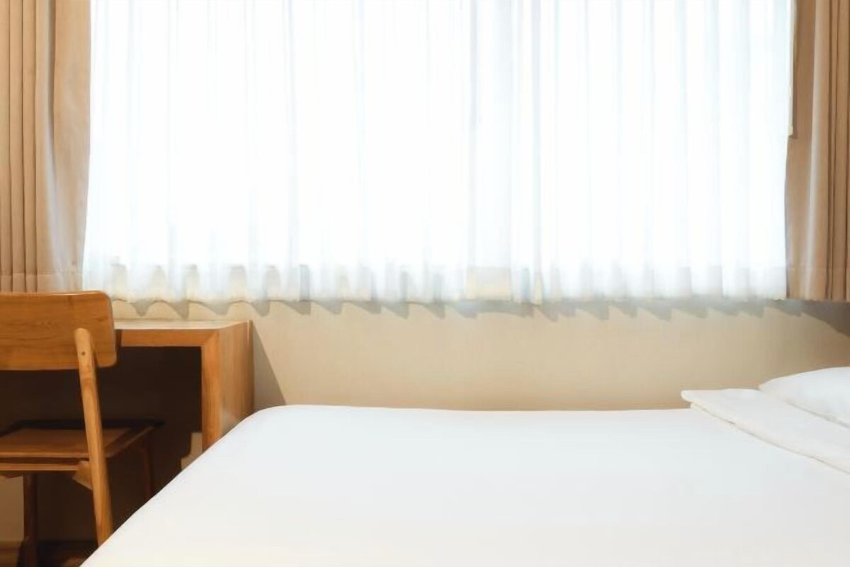 A hotel room with a bed, a wooden chair, and a small table.