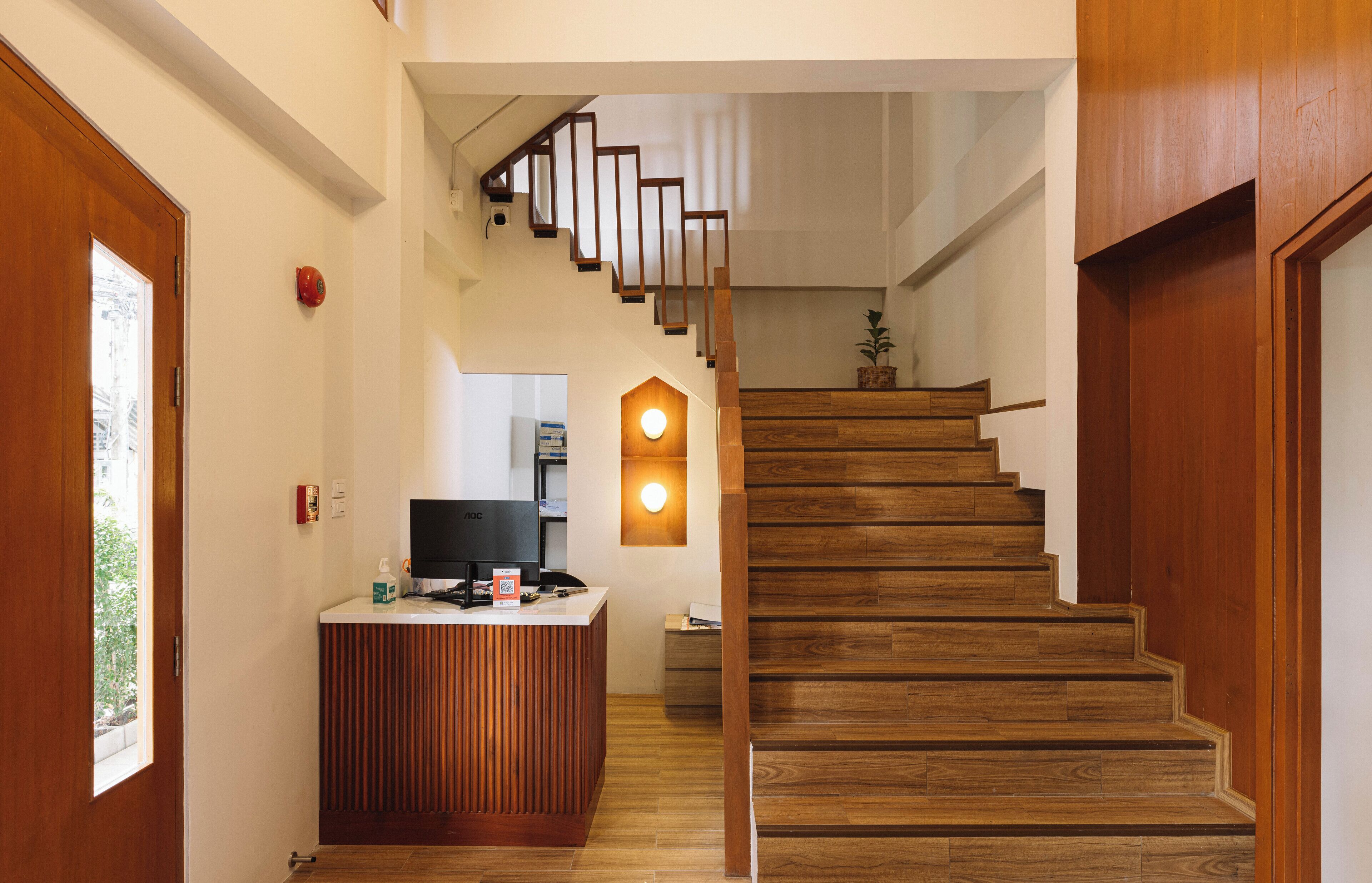 A modern reception desk with a flat-screen TV, wooden flooring, and a staircase with wooden steps and a metal railing.