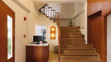 A modern reception desk with a flat-screen TV, wooden flooring, and a staircase with wooden steps and a metal railing.
