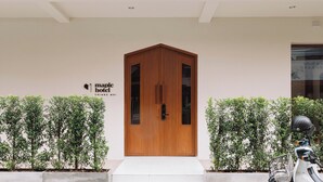 Una entrada de hotel moderna con una puerta de madera, un cartel que dice Maple Hotel y una moto estacionada afuera.
