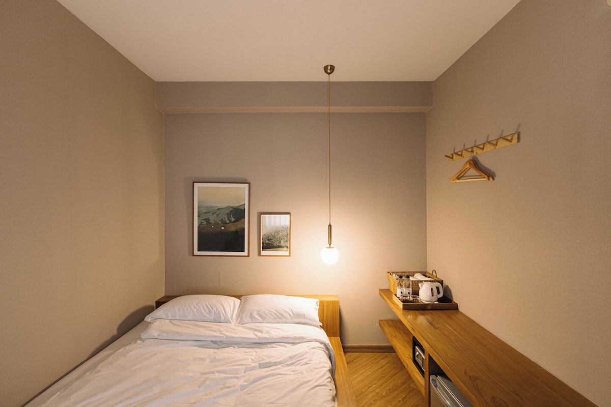 Une chambre à coucher avec un lit, une table de chevet avec une lampe et une étagère avec une bouilloire et un panier.