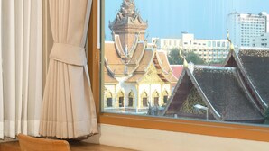 Una habitación con un escritorio de madera, una silla y un ventanal con vistas a arquitectura tradicional.