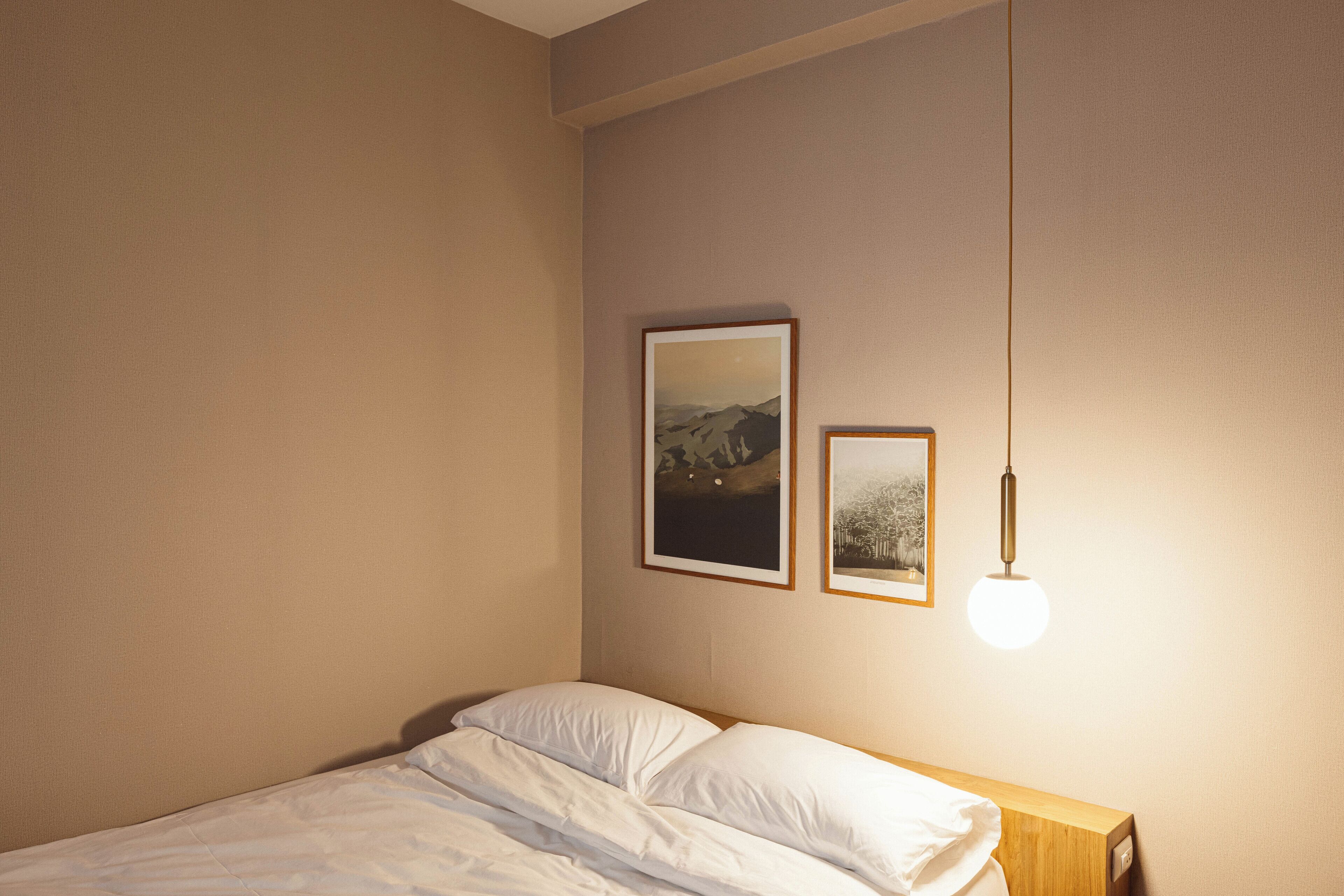 A neatly made bed with white linens in a room with beige walls. There are two framed pictures hanging on the wall above the bed.