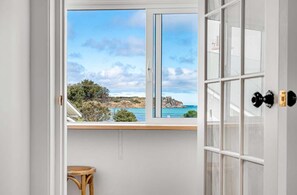 A room with a large window offering a coastal view, a wicker chair, and a white door with a black handle.