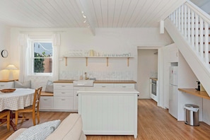 A modern kitchen with white cabinetry, a dining area with a table and chairs, and a staircase with a railing. - The Coach House, Esplanade Cottage, Dog Friendly (Victor Harbor)