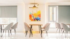 Zona pranzo moderna con tavolo bianco, quattro sedie e un quadro astratto colorato appeso alla parete.