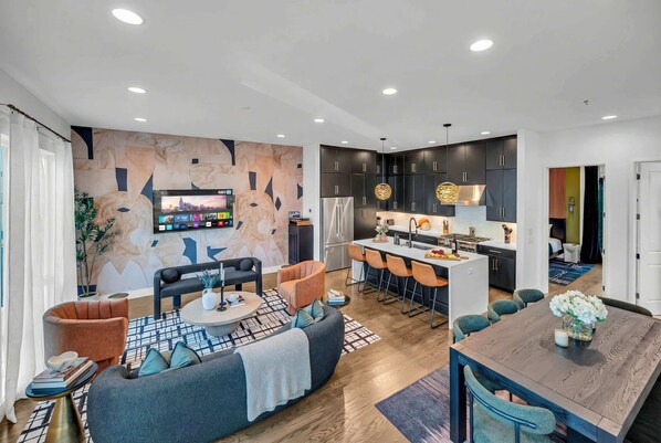 A modern living room with a sofa, coffee table, and TV. There is a kitchen area with a dining table and chairs.