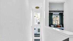 Una escalera moderna con paredes blancas y vista a un área de estar con cortinas verdes y una cama.