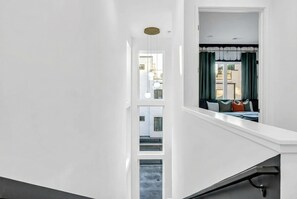A modern staircase with white walls and a view of a living area with green curtains and a bed.