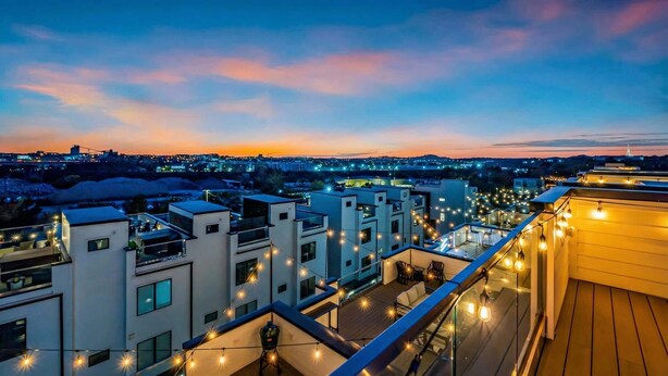 Un edificio moderno con varios balcones, luces cálidas y vistas a la ciudad al atardecer.