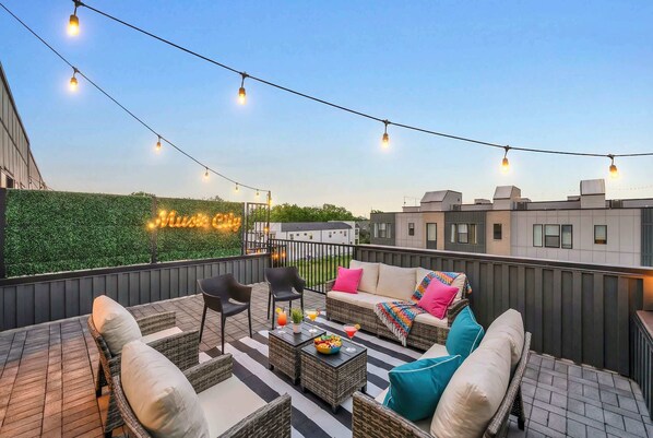 An outdoor patio area with wicker furniture, a table with a drink, and string lights.