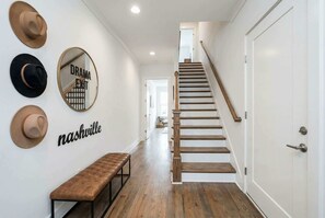 A hallway with a wooden staircase, a bench, and wall-mounted hats.
