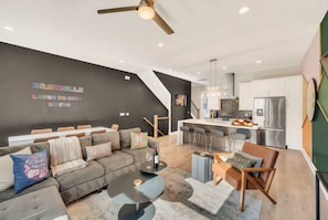 A modern living room with a sofa, coffee table, and a dining area with chairs and a kitchen in the background.