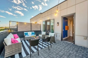 A rooftop patio with wicker furniture, a striped rug, and string lights.
