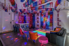 A room with a vibrant, colorful ceiling, a neon-lit floor, and a bar area with chairs and a sofa.