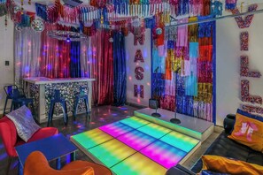 A room with a disco ball, colorful curtains, a bar area, and a seating area with a colorful floor.