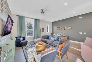 A modern living room with a grey sofa, a blue armchair, a green coffee table, and a TV mounted on the wall.