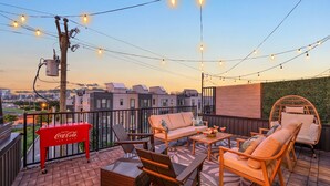 A rooftop terrace with outdoor seating, string lights, and a Coca-Cola cooler.
