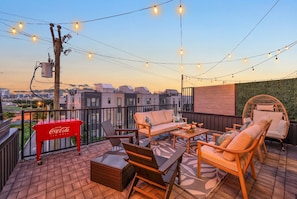 A rooftop terrace with outdoor seating, string lights, and a Coca-Cola cooler.
