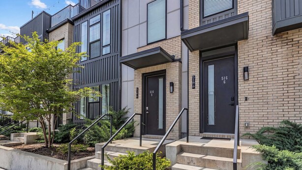 A modern multi-story residential building with a brick facade, large windows, and a black door with the number 516.