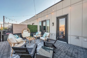 An outdoor seating area with modern furniture, a glass table, and string lights. - Festival season Nashville house: karaoke & ping pong room, sleeps 12 (Nashville)