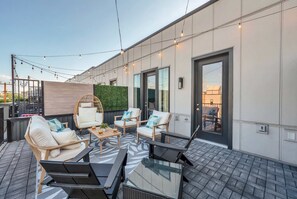 An outdoor patio with modern furniture, a glass table, and string lights.