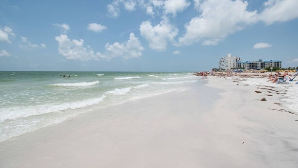 Ein Strand mit blauem Himmel, Wellen und einem Hotelkomplex im Hintergrund.