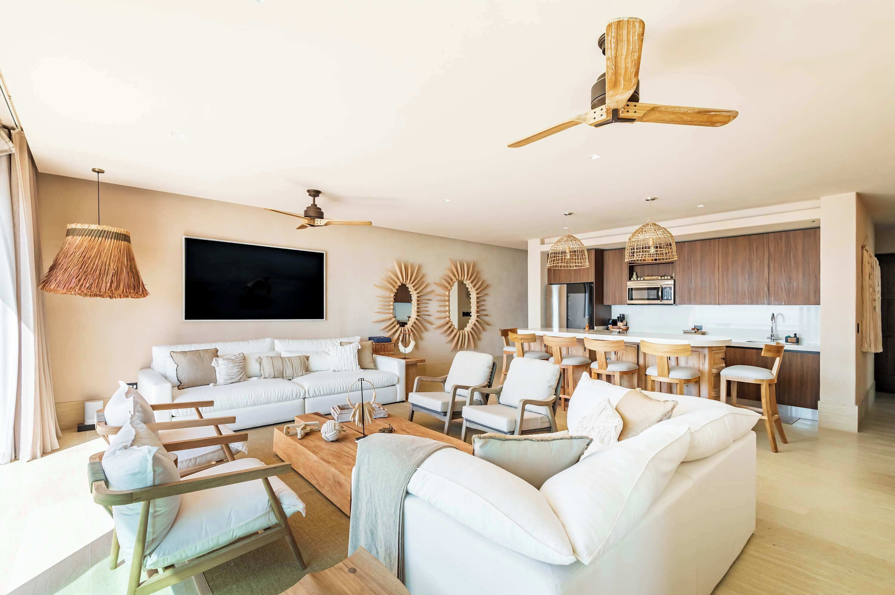 A modern living room with a sofa, chairs, a coffee table, and a TV. There is a kitchen area with a dining table and chairs.