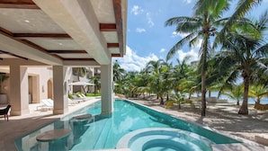 A swimming pool with a hot tub, surrounded by palm trees and lounge chairs, with a view of the ocean. - Artila PH: Seaview Oasis with Private Terrace and Direct Access to the Beach (Isla Mujeres)