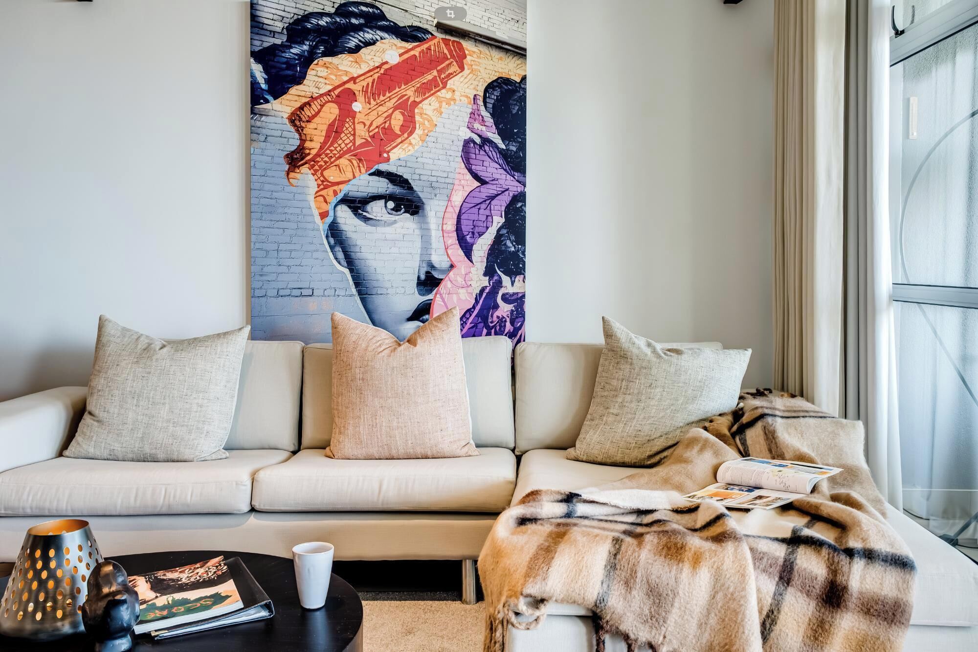 Un salon moderne avec un canapé beige, un grand tableau abstrait et un plaid en fourrure.