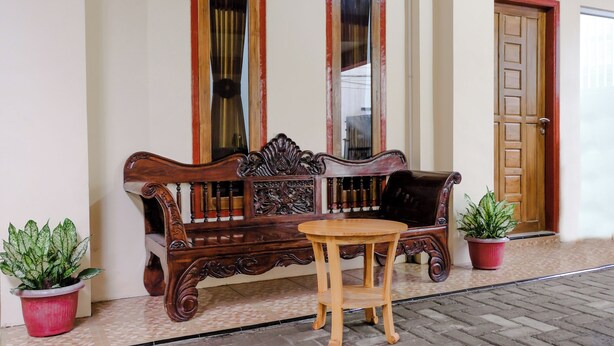 A wooden bench with intricate carvings, a small round table, and two potted plants. - Hotel O D&a Guesthouse Syariah And Rent Car (Malang)