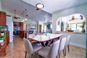 Une cuisine spacieuse dotée d’appareils électroménagers modernes, un coin repas avec une table en marbre et un salon confortable agrémenté d’une grande fenêtre et de plantes décoratives.