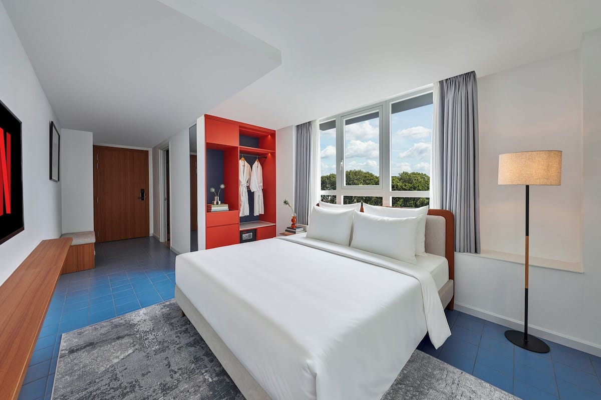 A hotel room with a large bed, a wardrobe, a desk, and a window with a view.
