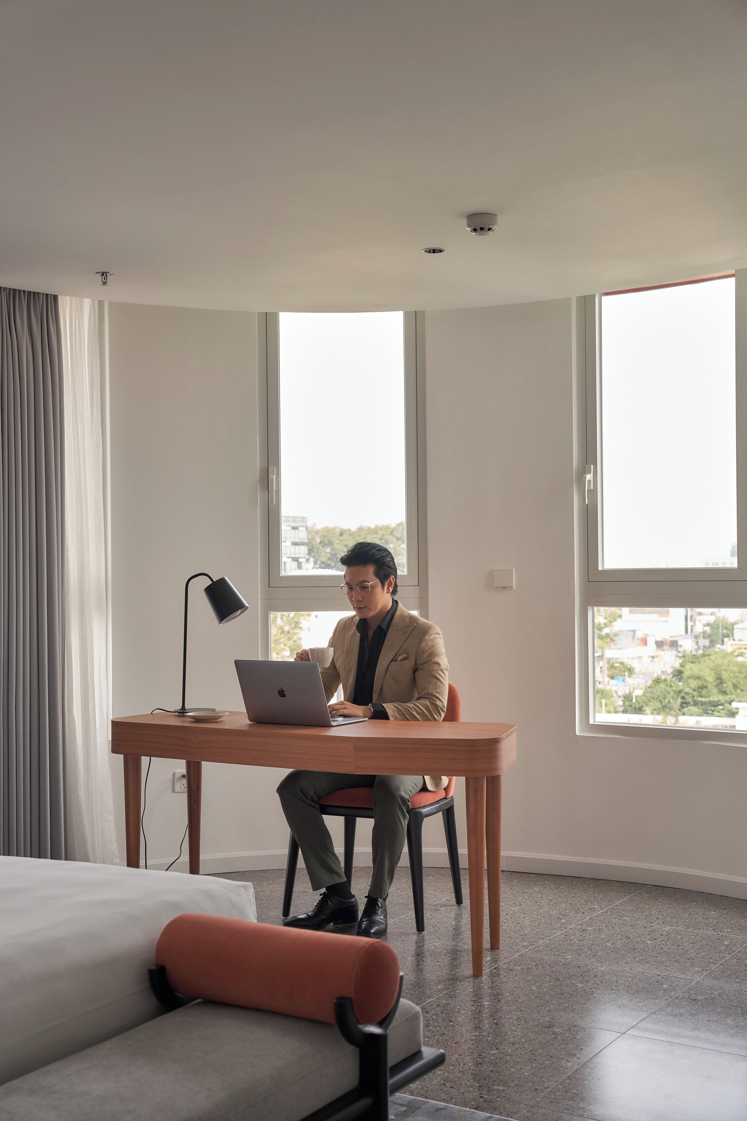 Une chambre d’hôtel moderne dotée d’une grande fenêtre, d’un bureau avec un ordinateur portable, d’un lit et d’une chaise.