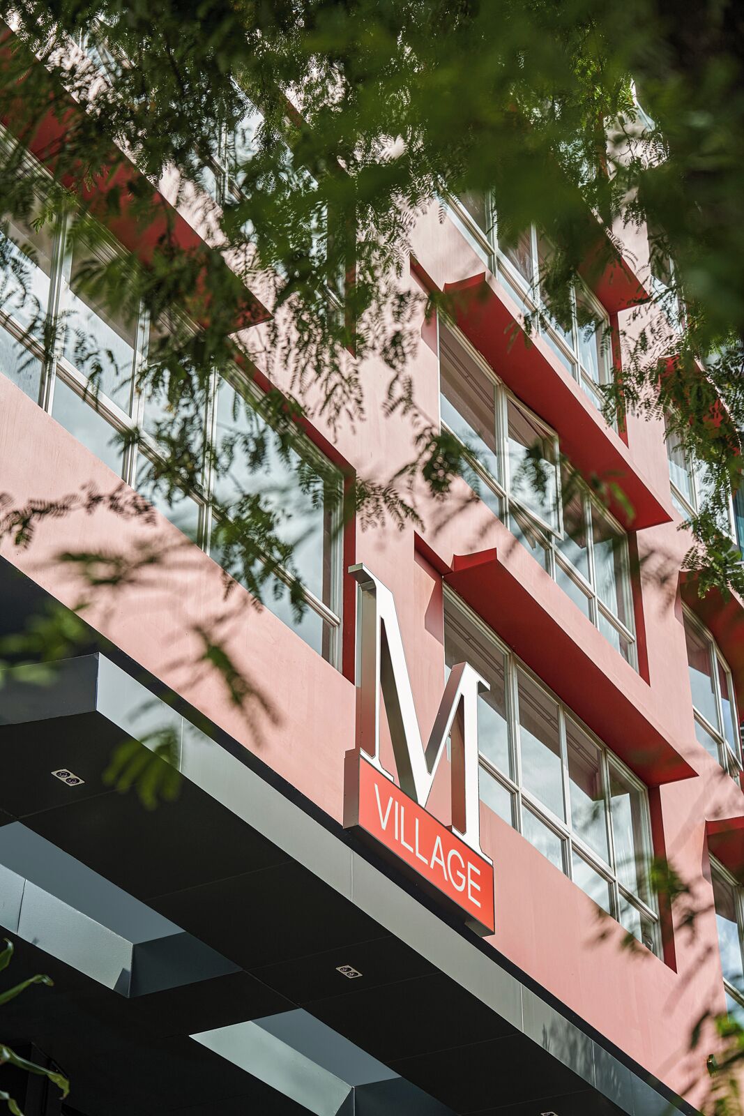 Een gebouw met een opvallend 'M Village' bord, grote ramen en een modern architectonisch ontwerp.