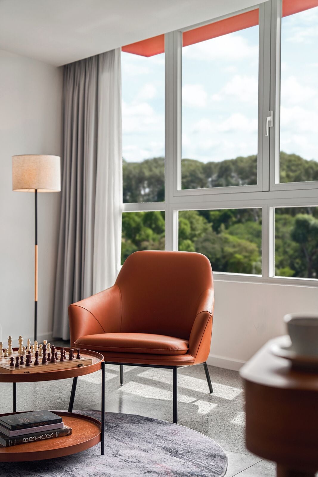 Ein modernes Zimmer mit Ledersessel, Schachbrett und Blick auf Grün hinter großen Fenstern.