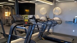 Ein Fitnessraum mit Laufbändern, Trainingsgeräten und einem Fernseher an der Wand.