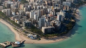 Luftaufnahme einer Küstenstadt mit dichter Hochhausbebauung, einem Strand und einem Bootsanleger.