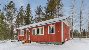 Eine rote Holzhütte mit schneebedecktem Dach, umgeben von hohen Kiefern.